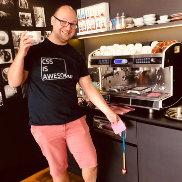 Lustiger Typ mit Kaffeetasse in der rechten Hand vor guter Kaffeemaschine