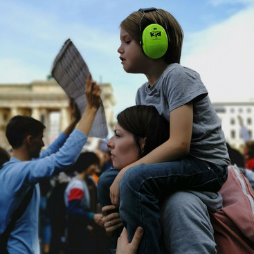 Ein Kind mit grünem Gehörschutz sitzt auf den Schultern einer Frau auf einer Demonstration